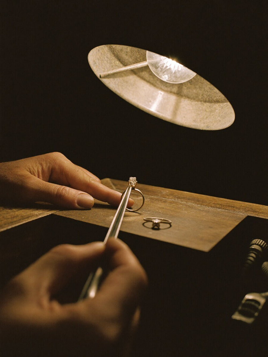 A maker's hands setting a stone under a workbench lamp