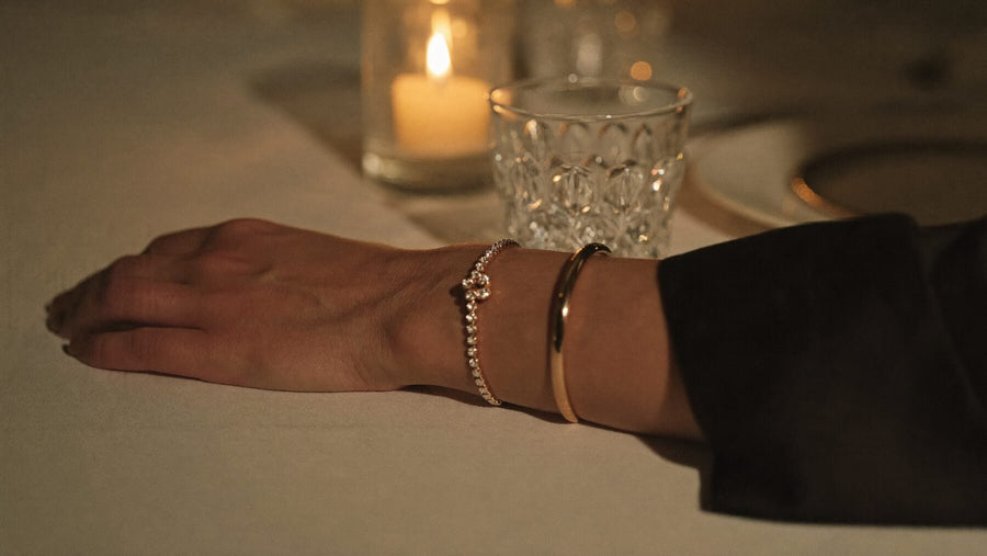 At a candlelit dinner, a wrist rests on white linen wearing a diamond bracelet