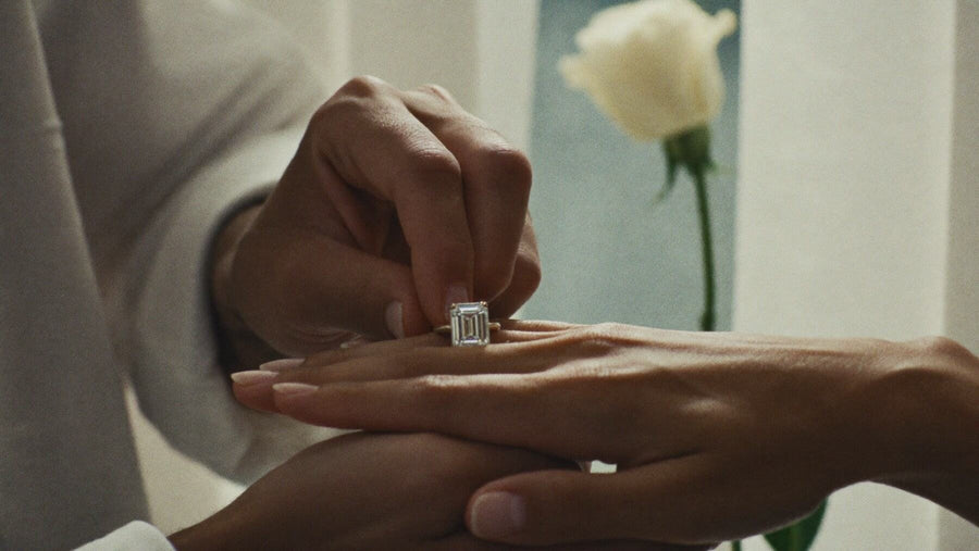 A diamond ring being placed on a woman’s finger beside a white rose